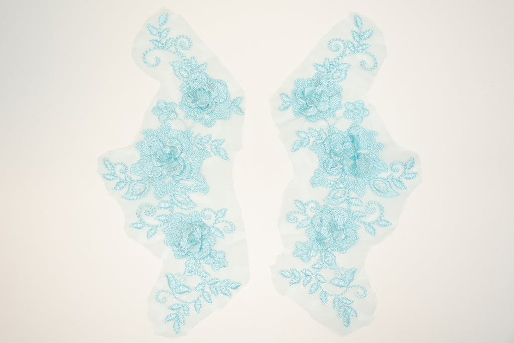 Pair of light blue floral lace appliqués on a white background