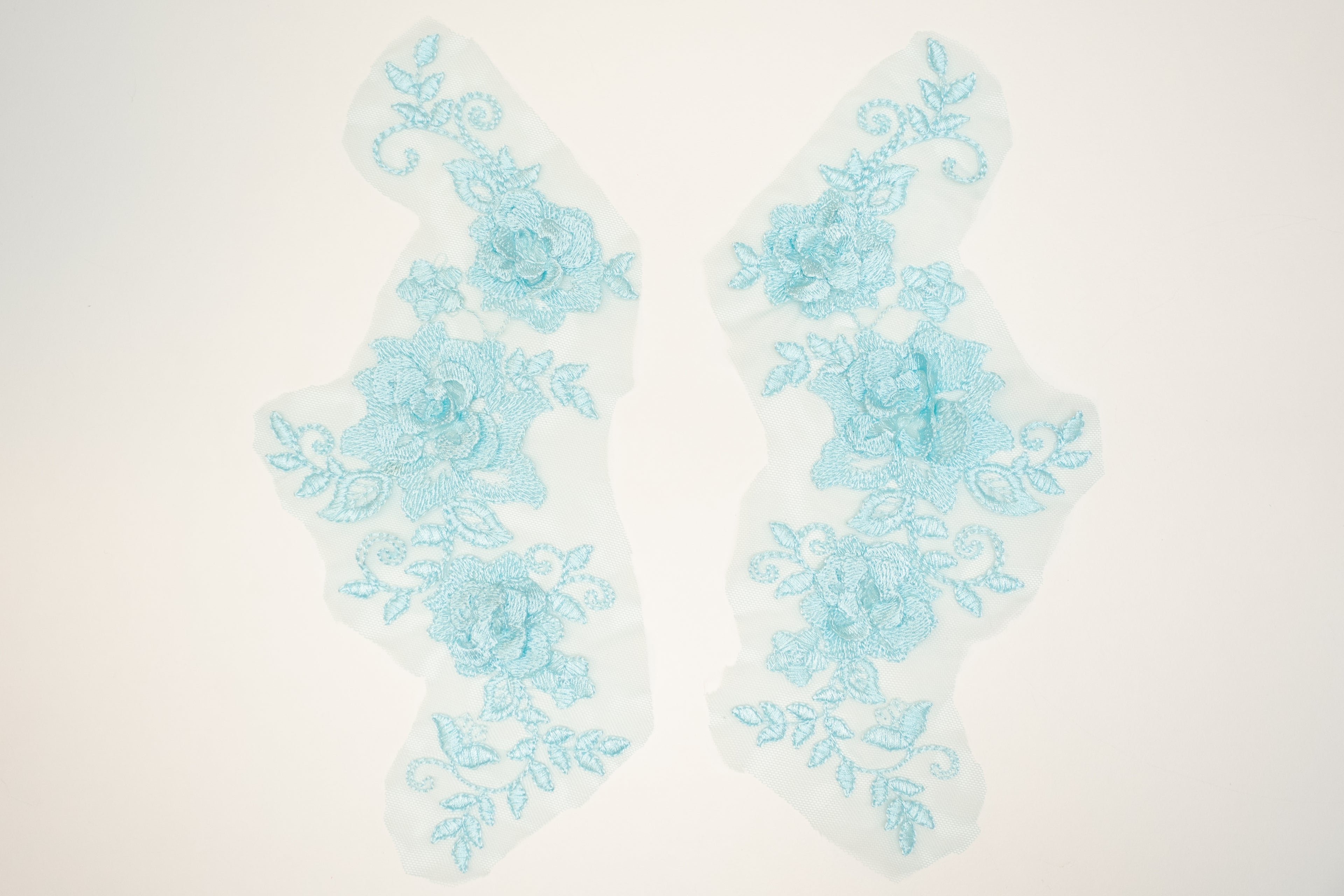 Pair of light blue floral lace appliqués on a white background