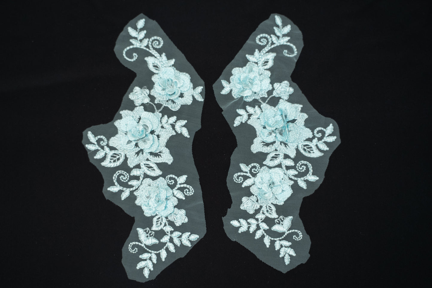 Pair of light blue floral lace appliqués on a black background