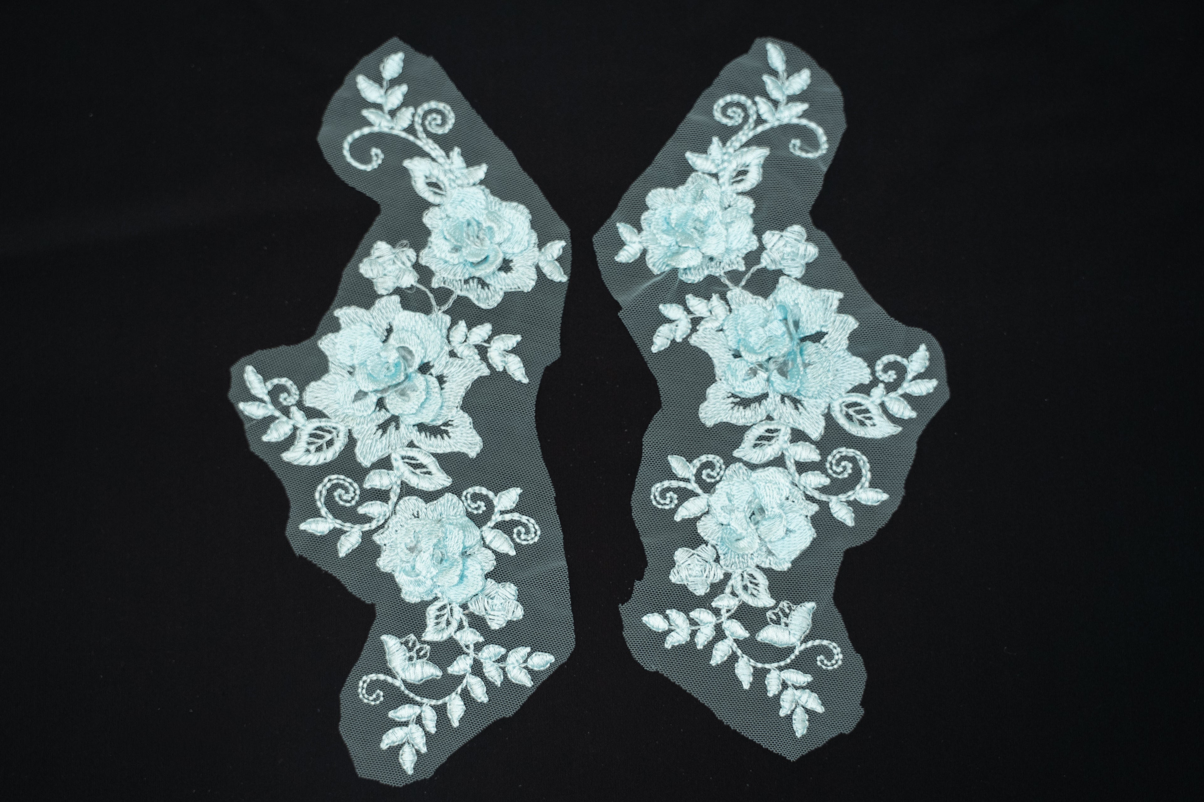Pair of light blue floral lace appliqués on a black background