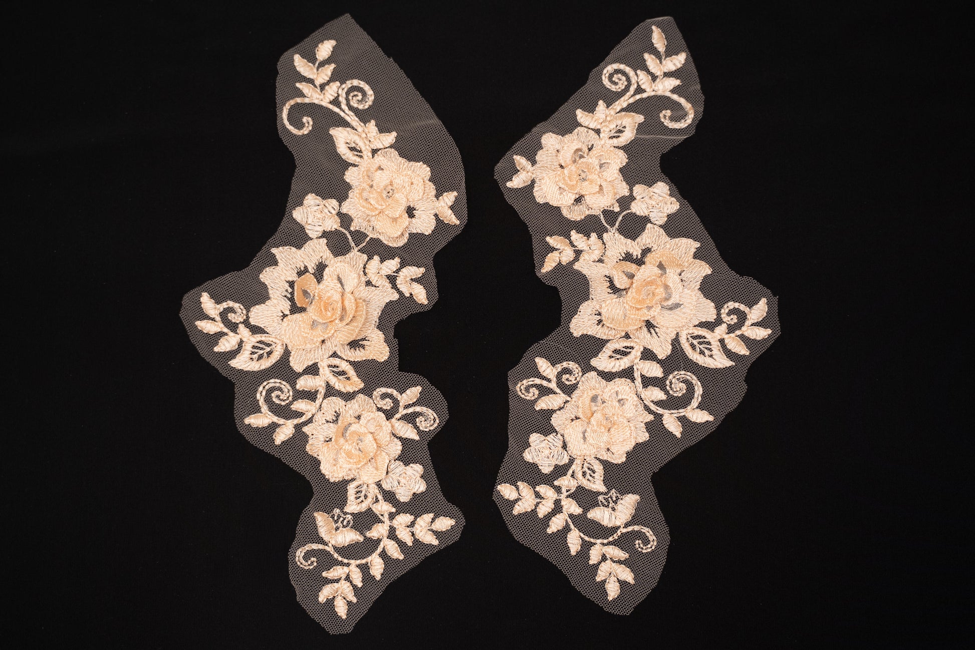 Pair of beige floral lace appliqués on a black background