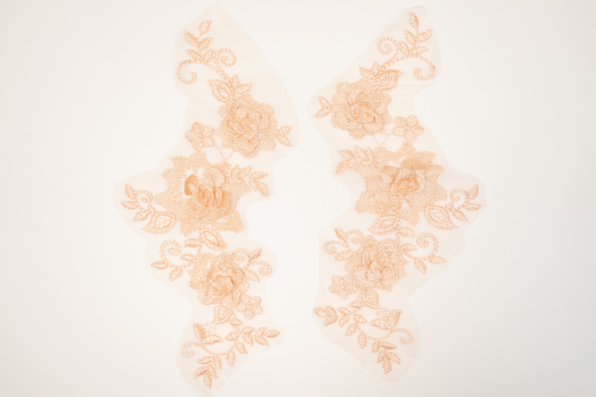 Pair of peach-colored lace appliqués on a white background
