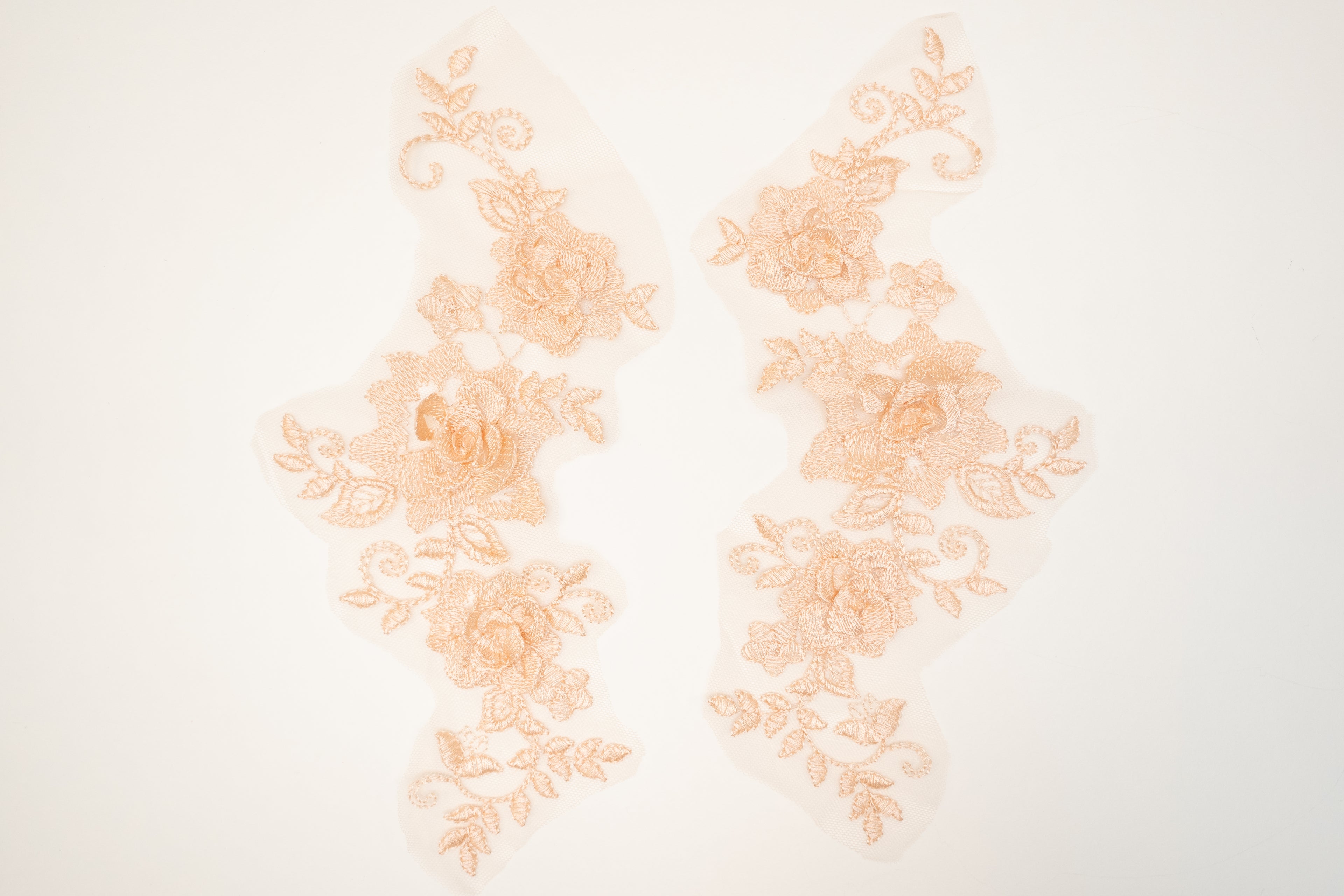 Pair of peach-colored lace appliqués on a white background
