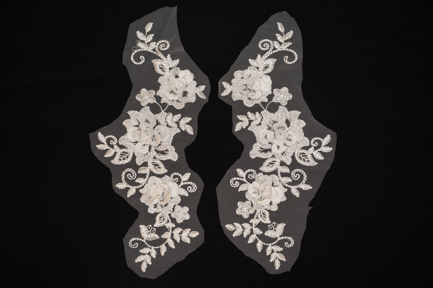 Pair of white lace shoe covers with floral patterns on a black background