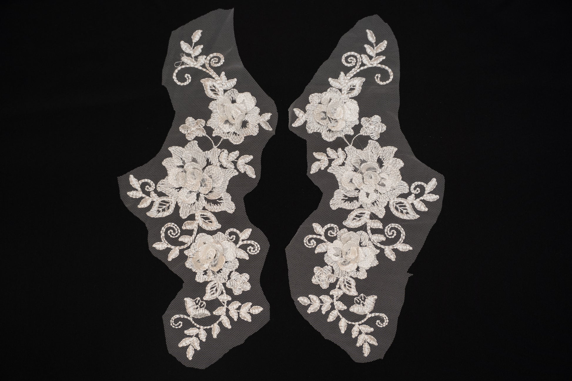 Pair of white lace shoe covers with floral patterns on a black background