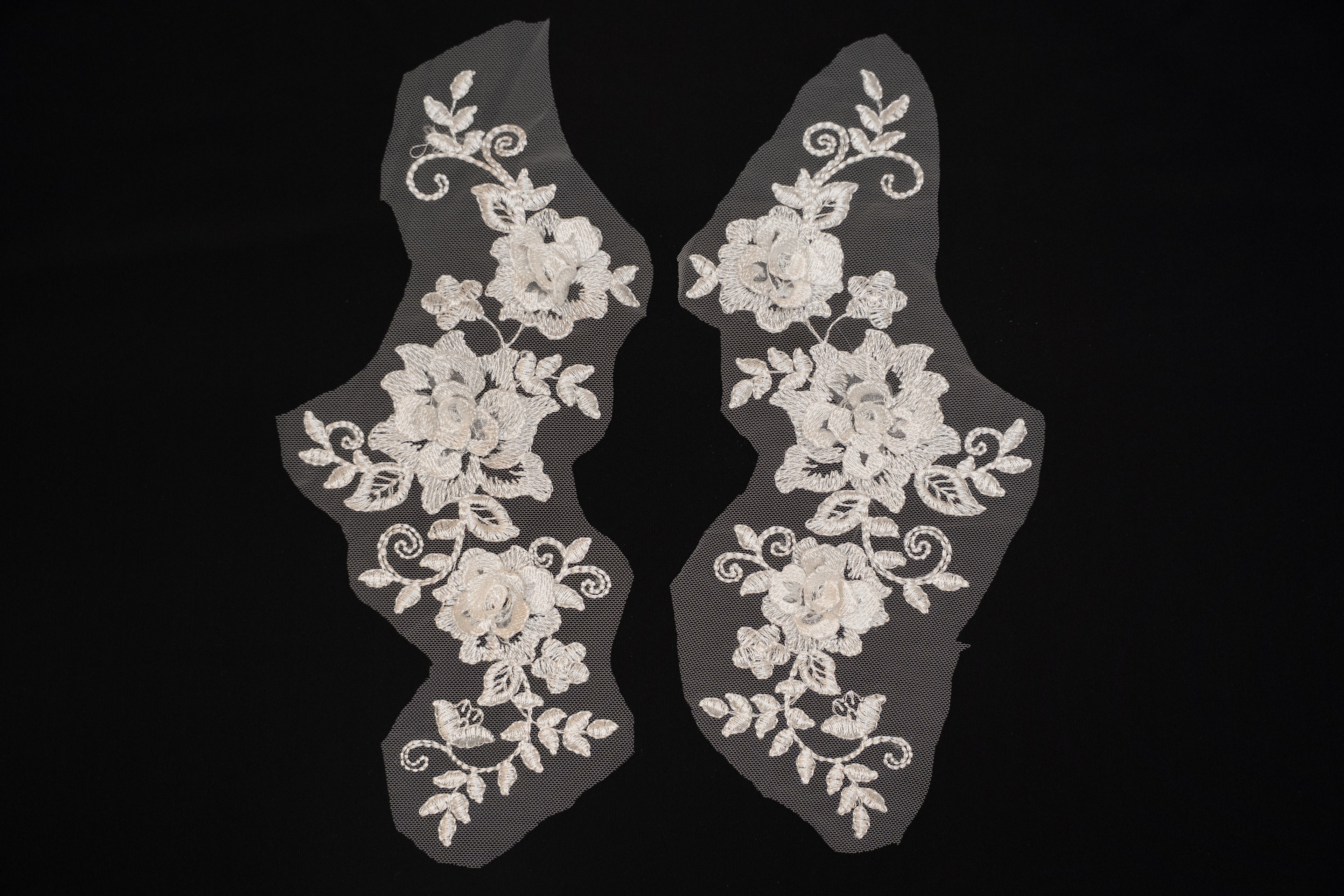 Pair of white lace shoe covers with floral patterns on a black background