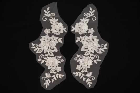 Pair of white lace shoe covers with floral patterns on a black background