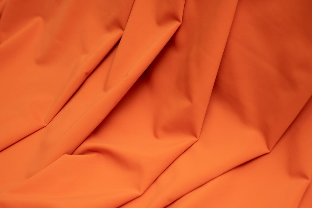 A close-up of draped orange fabric with soft folds and a smooth texture filling the frame.