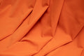 A close-up of draped orange fabric with soft folds and a smooth texture filling the frame.