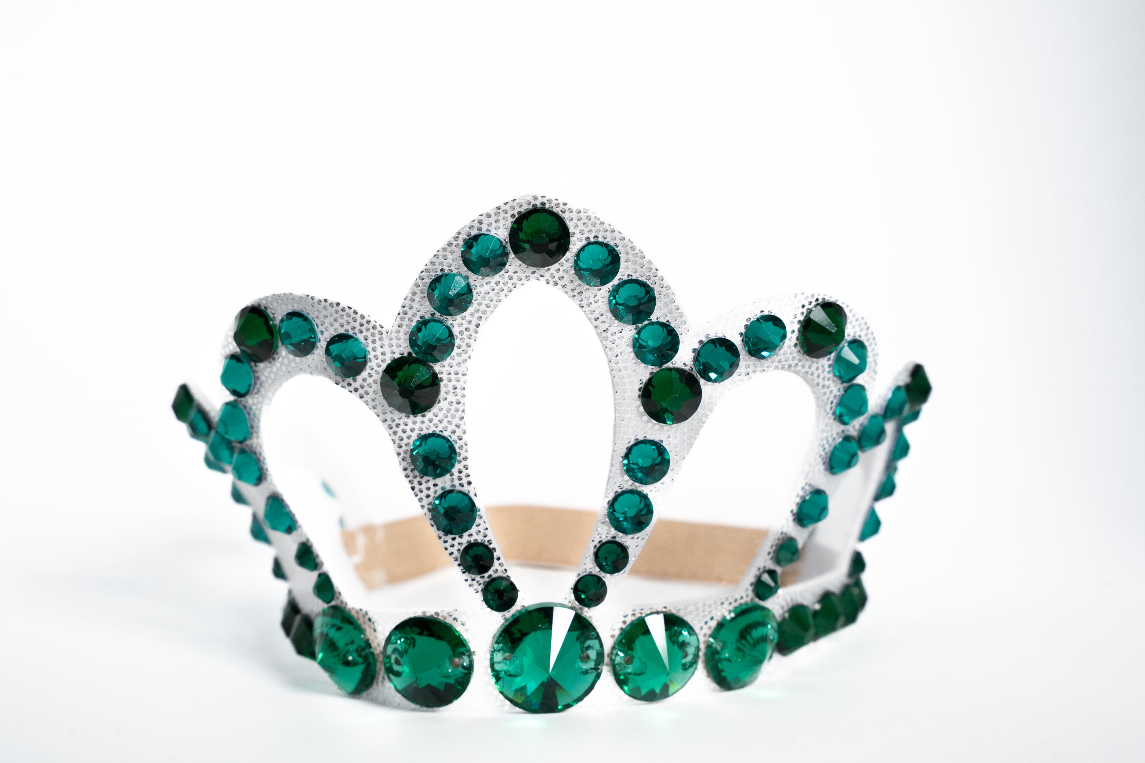 White tiara with green gemstones on a white background