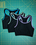 Black sports bras with colorful trim on a green cutting mat