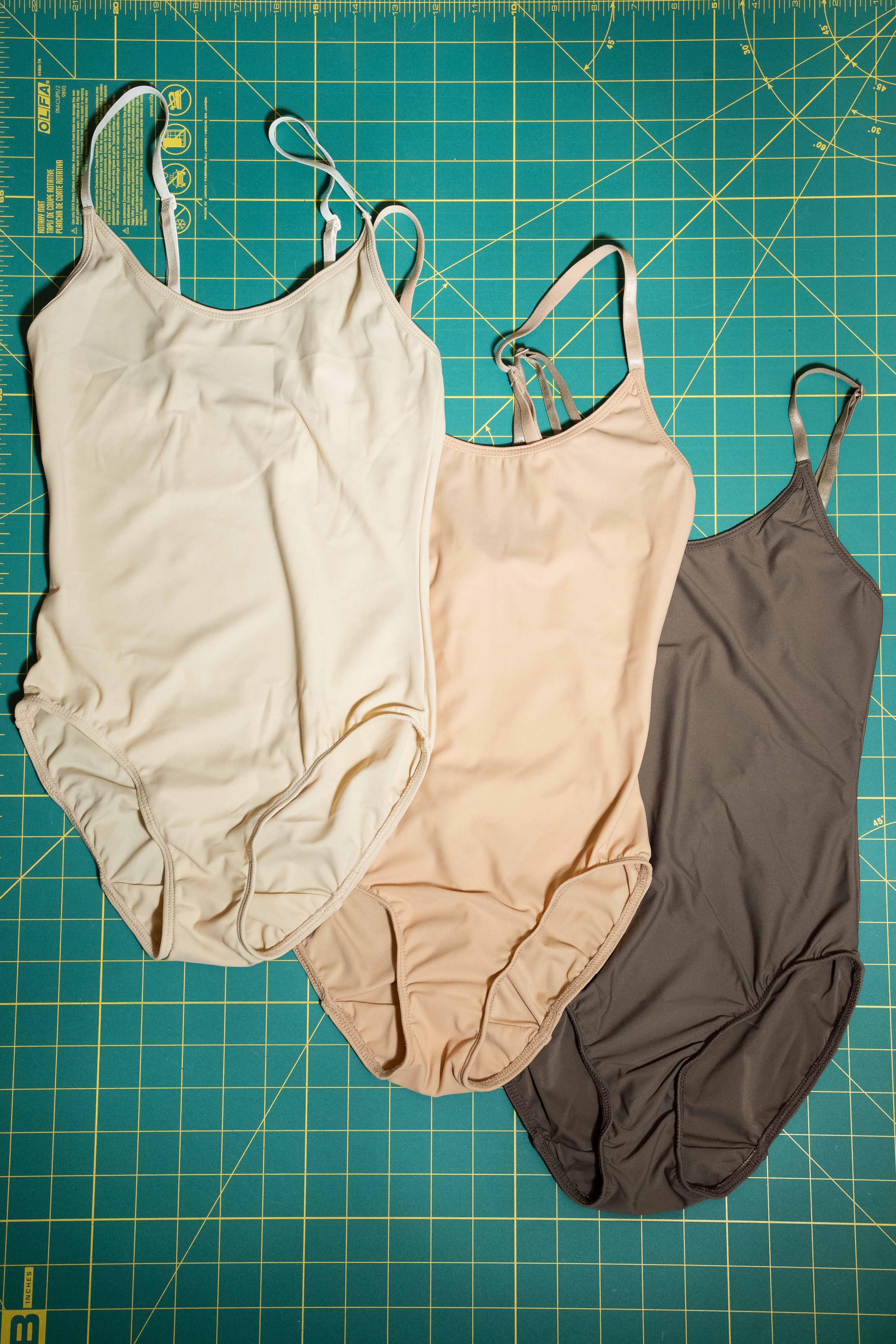 Three swimsuits in beige, pink, and brown on a grid-patterned surface.