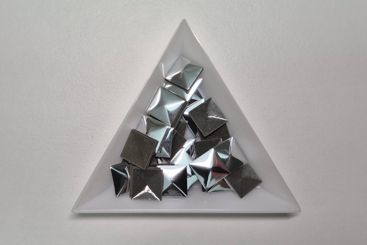 Triangular white dish with metallic pyramid-shaped objects on a light gray background