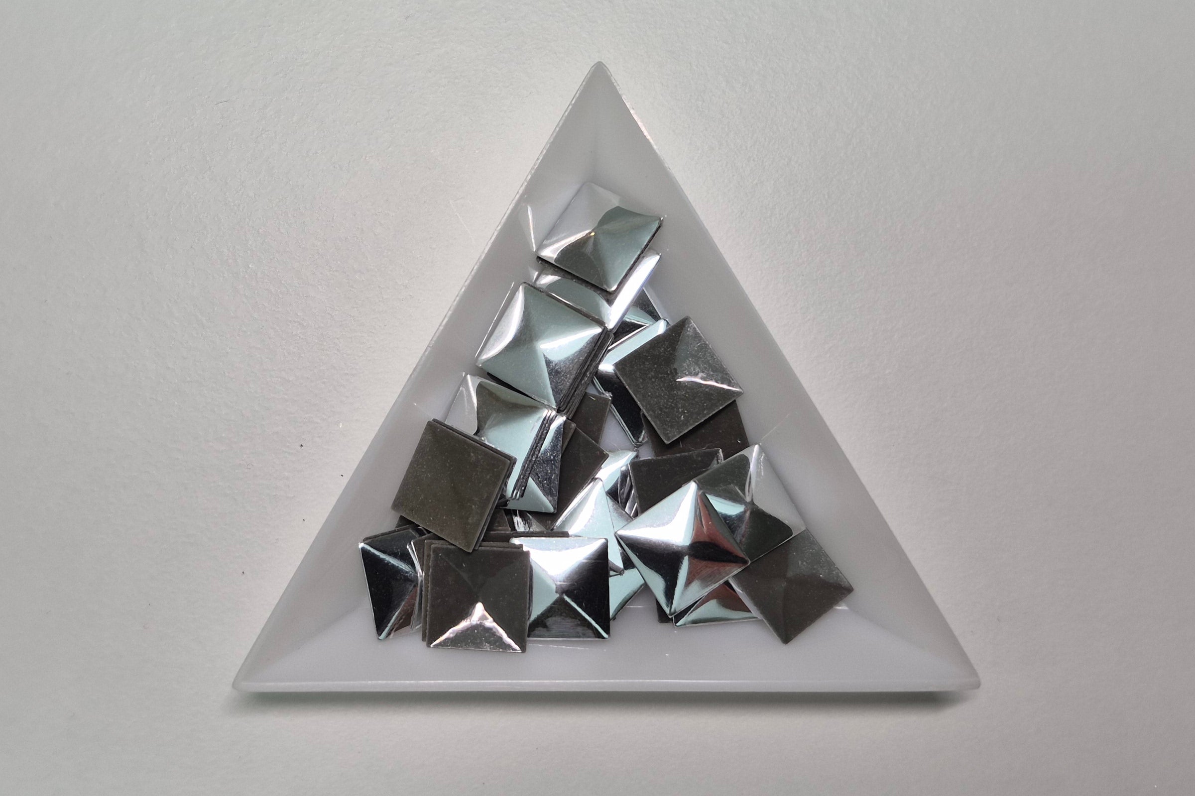 Triangular white dish with metallic pyramid-shaped objects on a light gray background