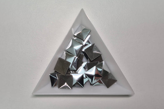 Triangular white dish with metallic pyramid-shaped objects on a light gray background