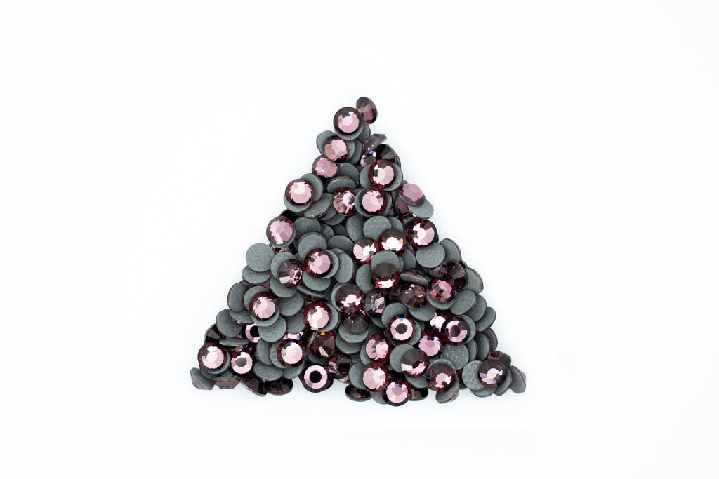 A pile of small round sequins arranged in a triangle shape on a plain white background. The sequins have dark gray to black backs with shiny pink and mauve-purple fronts.