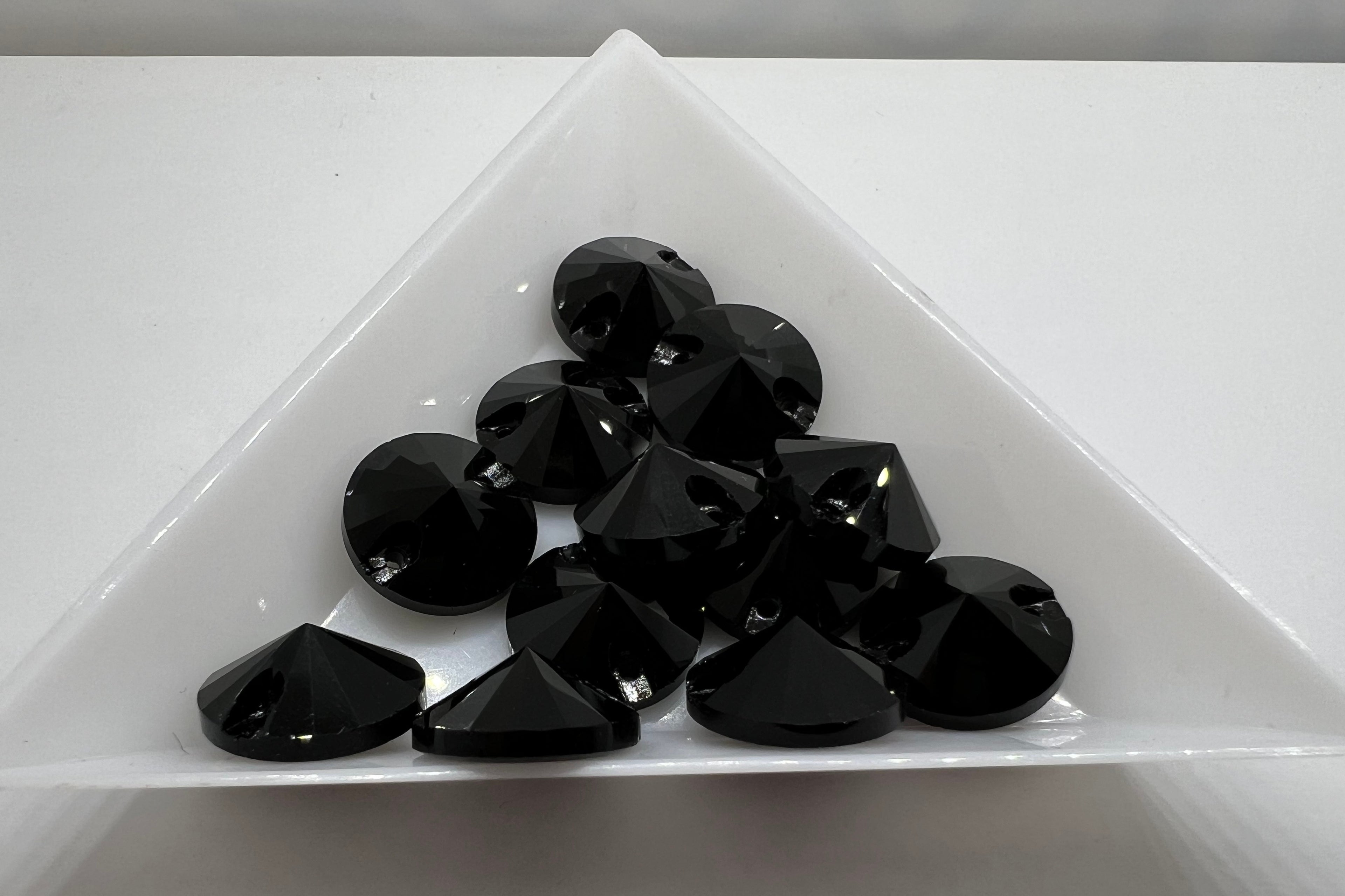 A collection of small, jet black, round sew-on rhinestones arranged in a triangular pattern on a white surface.